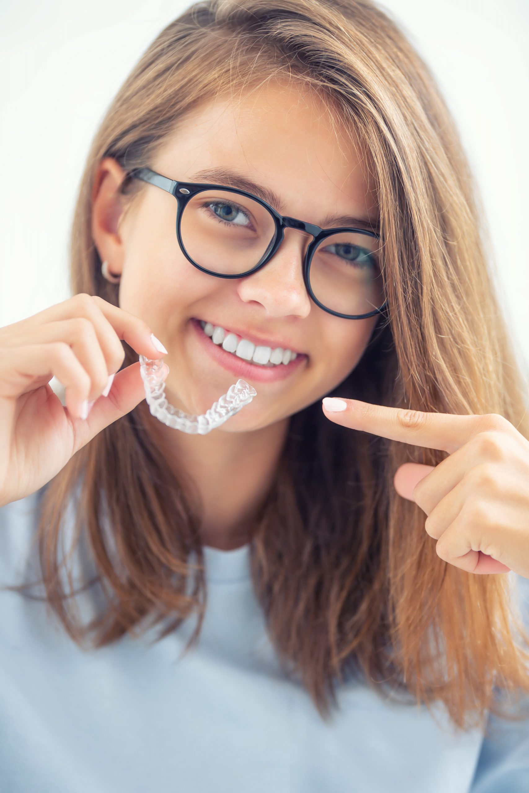 Dental invisible braces or silicone trainer in the hands of a young smiling girl. Orthodontic concept – Invisalign.
